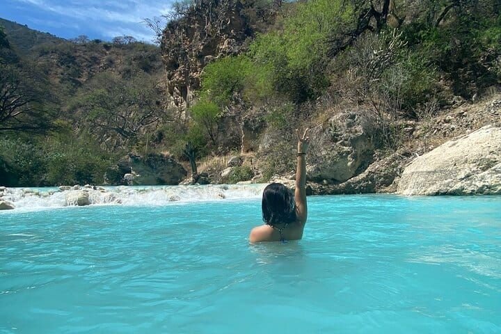Una bañista con el brazo en alto en el agua turquesa del río