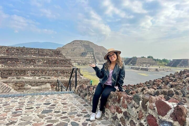 A guest posing on a stone wall with the Pyramid of the Moon behind