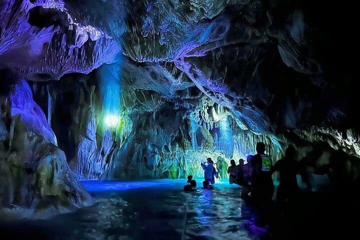 El interior de la gruta iluminado en azul y violeta, con visitantes en el agua