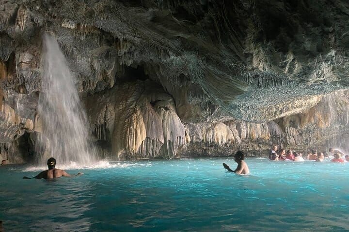 Una cascada interior cayendo sobre la poza turquesa de la gruta